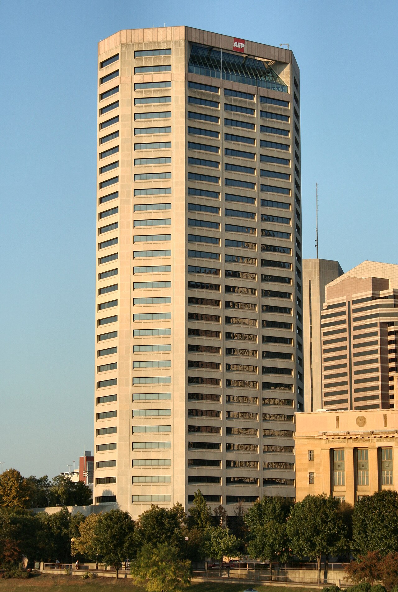 A tall glass office tower with the red AEP logo at the top, seen from street level against a blue sky.