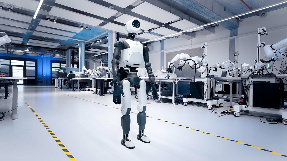 A compact white and grey humanoid standing in a bright robotics laboratory.