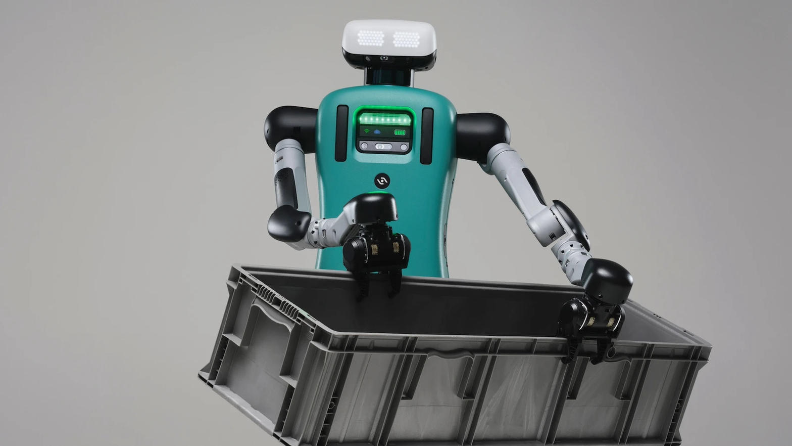 Agility Robotics’ Digit humanoid, teal and white, holding a grey plastic tote against a plain background.