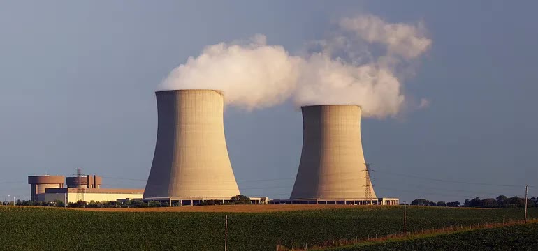 Two large concrete cooling towers at a nuclear station, one trailing steam, with fields in the foreground.