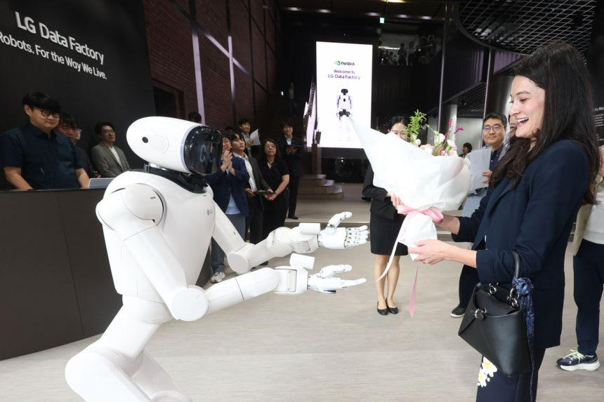 A white LG CLOiD humanoid reaches toward Madison Huang, who is holding a bouquet, inside the LG Data Factory.