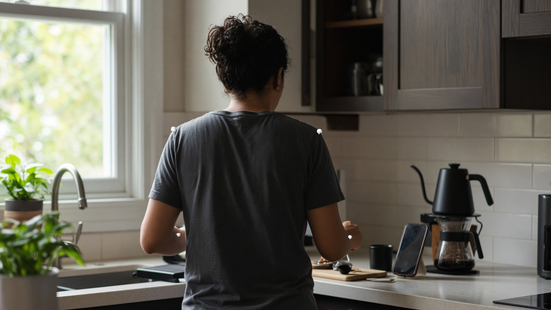 A person seen from behind, wearing small sensors, making coffee at a kitchen counter.