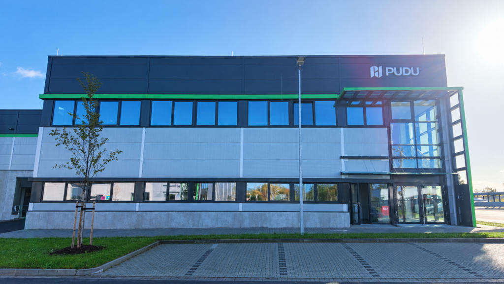 A two-storey commercial building in daylight, with the Pudu logo on the dark upper facade and a glass entrance.