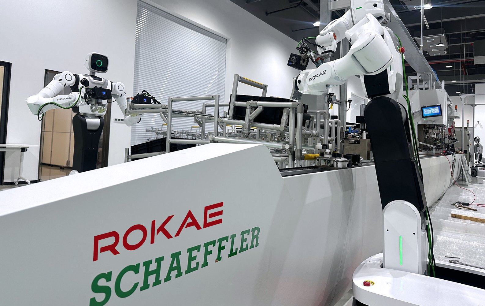 A wheeled humanoid and a large white arm on a factory line marked ROKAE and Schaeffler.