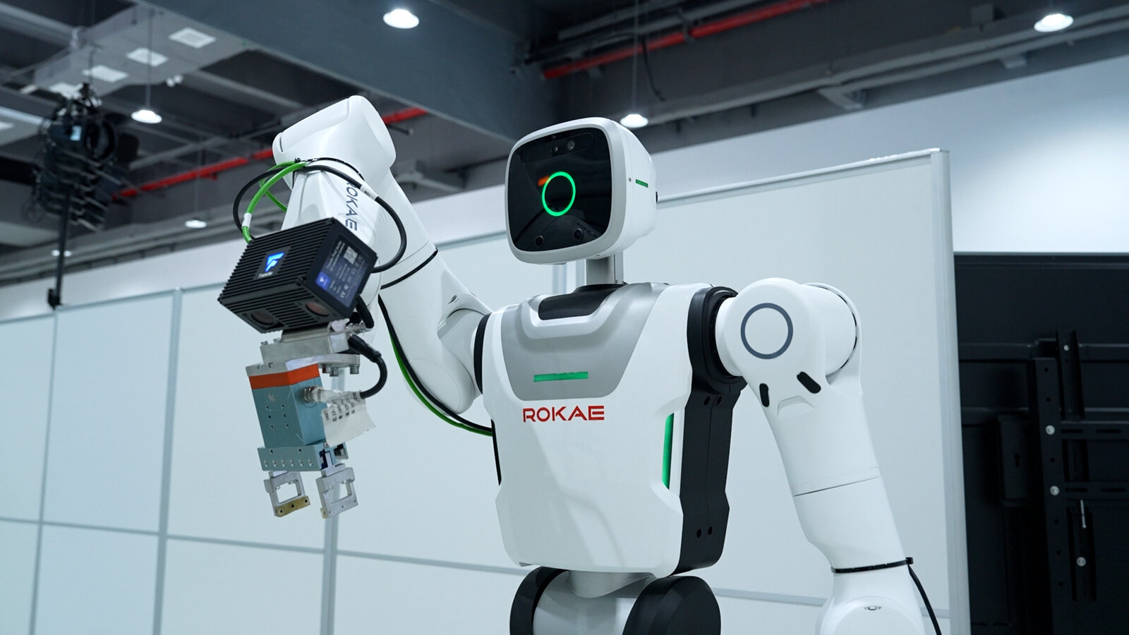 A white humanoid robot marked ROKAE holding a machined part in a bright factory.