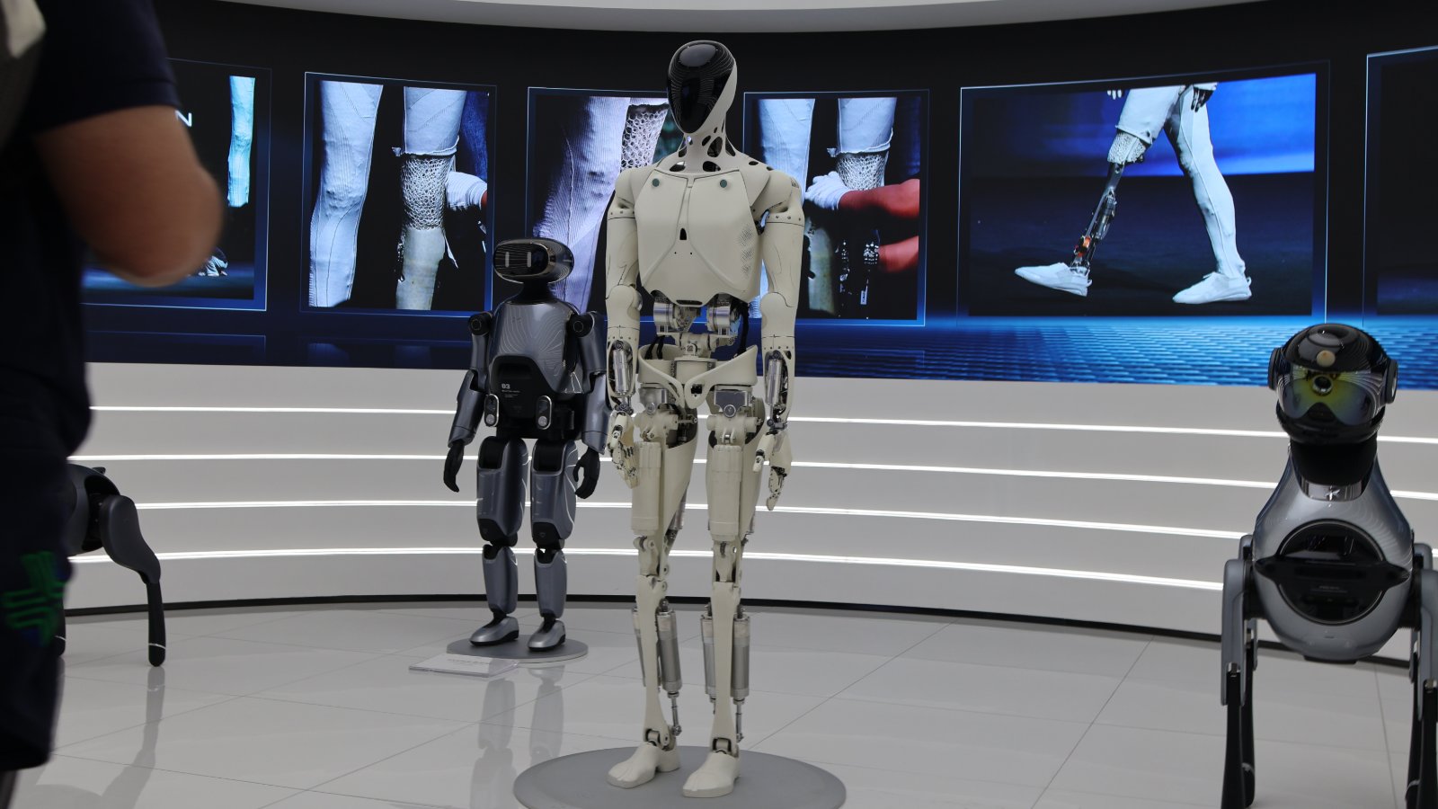 XPENG’s white IRON humanoid on a display stand, with a smaller robot and a robot dog beside it.